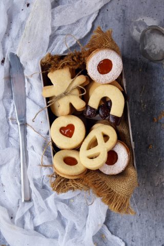 Biscotti senza glutine con farine naturali ripieni di marmellata di albicocche e ricoperti di cioccolato fondente e zucchero a velo